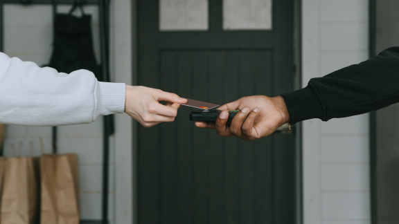 Close-up dos braos de duas pessoas estendidos na frente um do outro. Uma pessoa segura um carto de crdito e a outra uma mquina de carto.