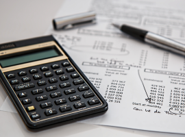 Foto de uma calculadora financeira em cima de uma folha cheia de contas e uma caneta representando o tema de frente de caixa.