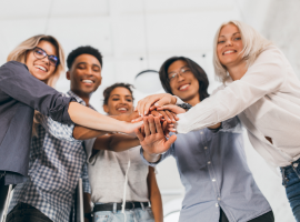 Imagem de um grupo com diversidade de gnero no ambiente de trabalho juntando as mos ao centro e sorrindo.