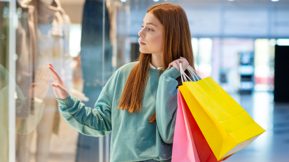 Mulher ruiva andando no shopping vendo como montar vitrine de loja enquanto segura sacola de compras.