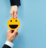 Duas mos segurando imagem de emoji com sorriso feliz, representando o que  psicologia positiva.