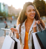 Imagem de uma mulher negra, de cabelos encaracolados e compridos, carregando vrias sacolas de compras para exemplificar o que  valor agregado.