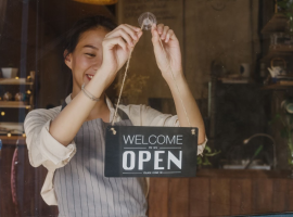 Empreendedora que entende de gesto de pequenas empresas colocando placa de ?aberto? na porta de sua loja.