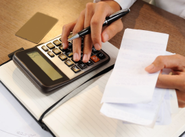 Close-up de empregador calculando em uma calculadora o pagamento de salrio dos colaboradores. Ele segura uma caneta em uma mo, e na outra, alguns recibos.