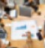 Grupo de pessoas reunido em torno de uma mesa, na qual h notebooks, pranchetas, papis, celulares e copos. A imagem representa uma reunio de estratgias de marketing.